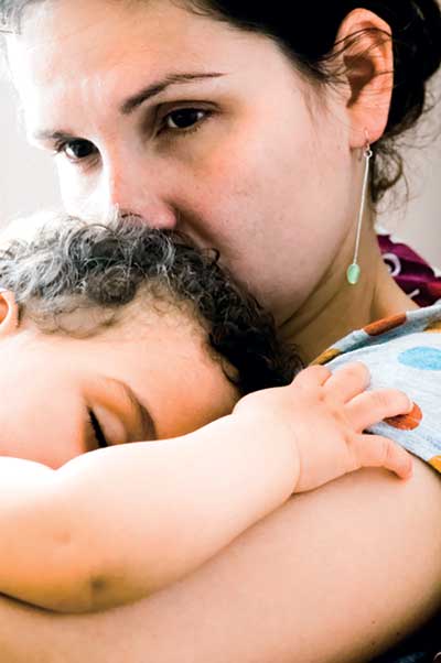 La madre sostiene a su bebé dormido. Parece preocupada y se inquieta