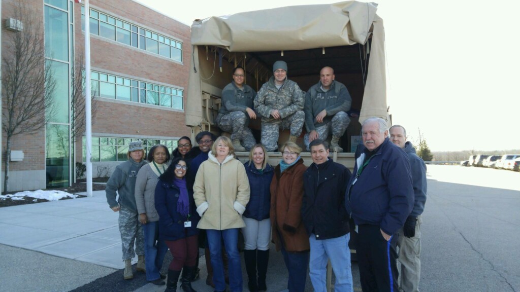 Staff and military members posing with truck outside of office building